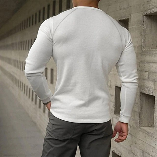 Person wearing a white long-sleeve shirt and dark pants against a concrete wall.