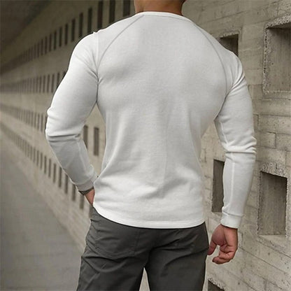 Person wearing a white long-sleeve shirt and dark pants against a concrete wall.