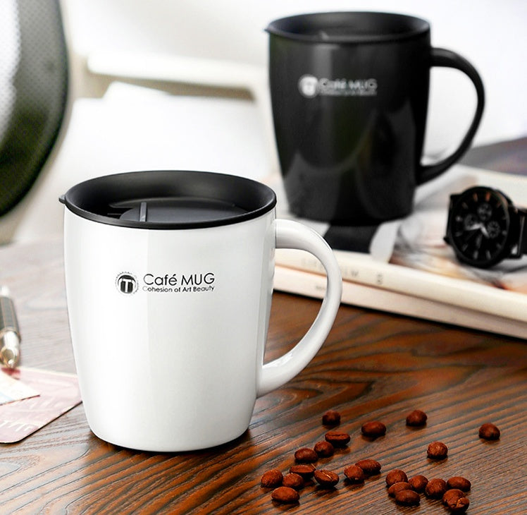 White mug with black lid on a wooden surface with scattered coffee beans, next to a black mug.